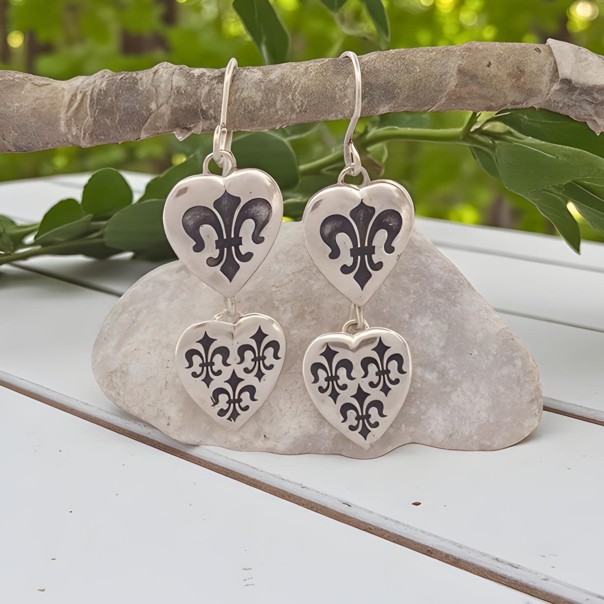 Heart-shaped earrings with black designs hanging on a branch with green leaves in the background.