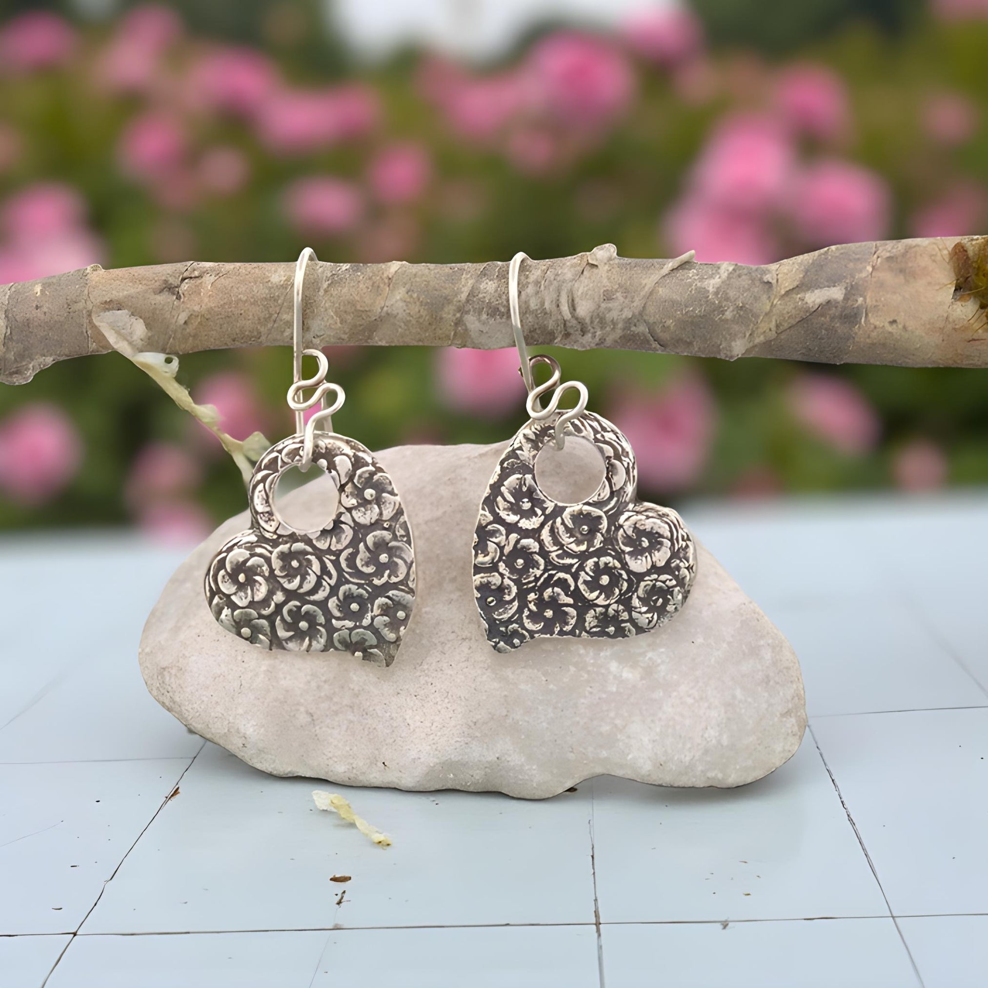 Silver floral earrings hanging on a branch with pink flowers in the background