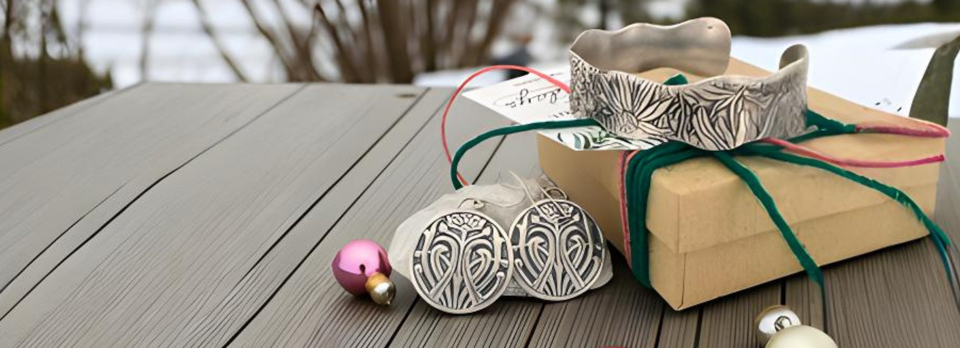 Decorative silver pieces and a gift box on a wooden surface with a blurred natural background