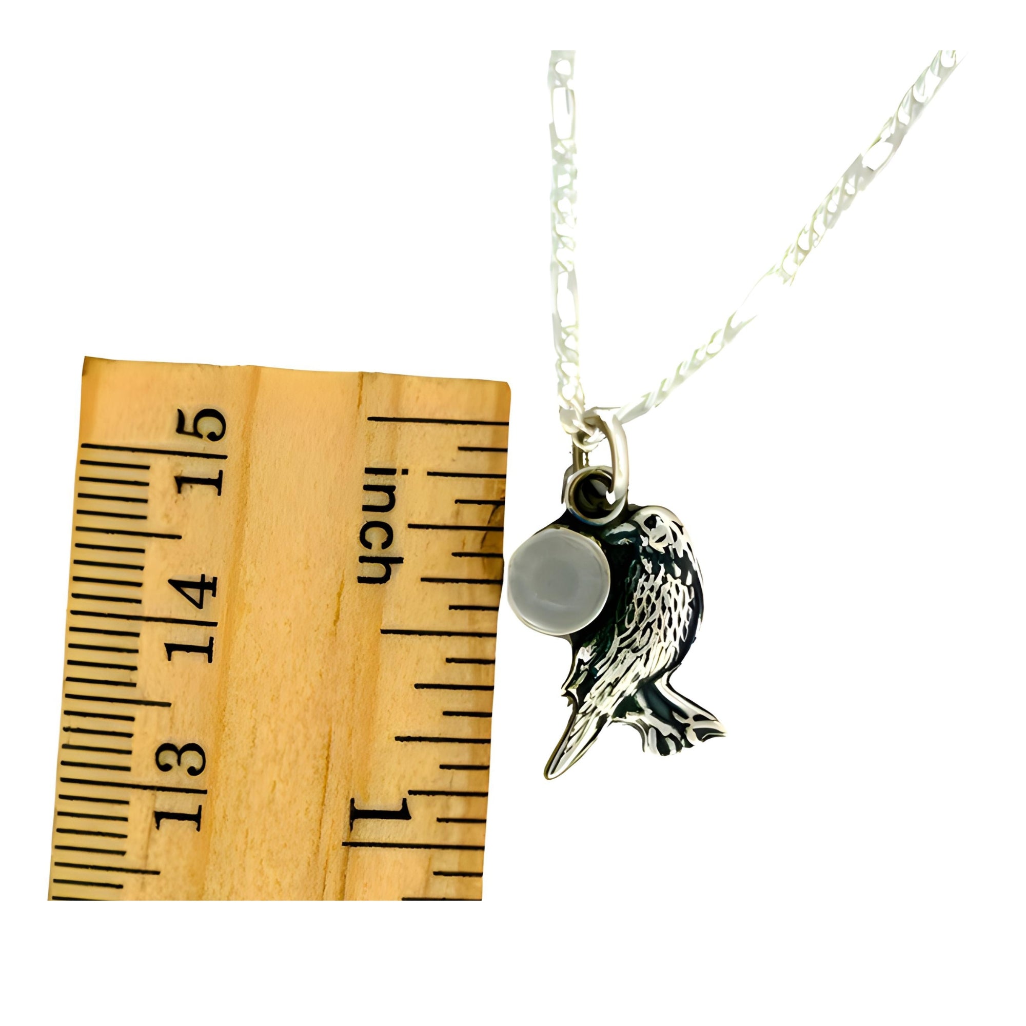 Bird-shaped pendant on a chain next to a wooden ruler for scale